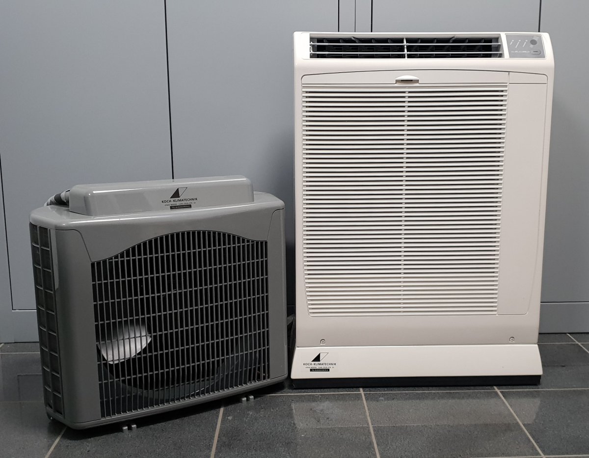 Zwei Klimageräte von KOCH-KLIMATECHNIK – ein graues Außengerät und ein weißes Innengerät – nebeneinander aufgestellt in einem Technikraum.
